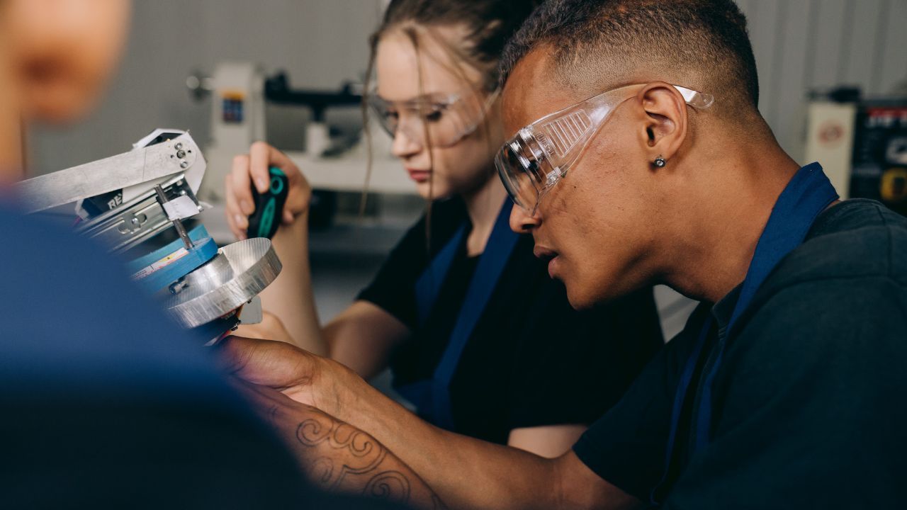 Two people wearing PPE working on a piece of mechanical equipment.