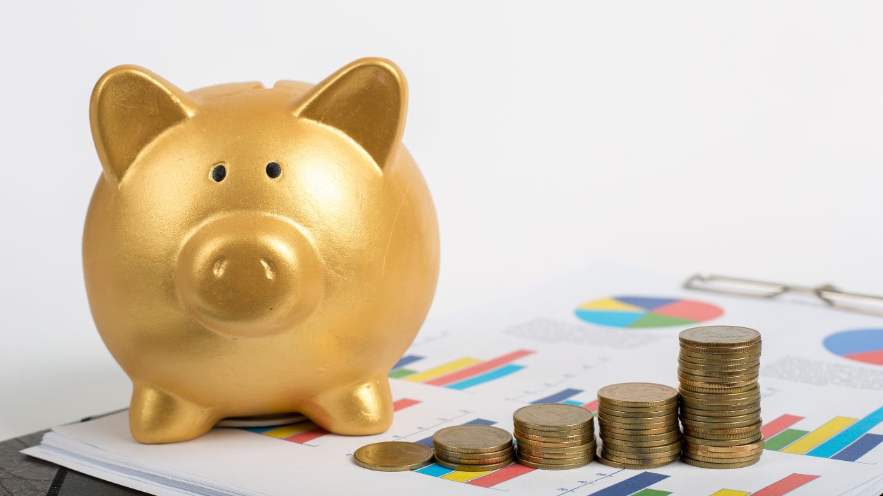 A golden piggy bank on top of a data sheet next to a gradually increasing pile of coins.