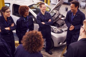 Six apprentices stood together with a mentor in a car garage.